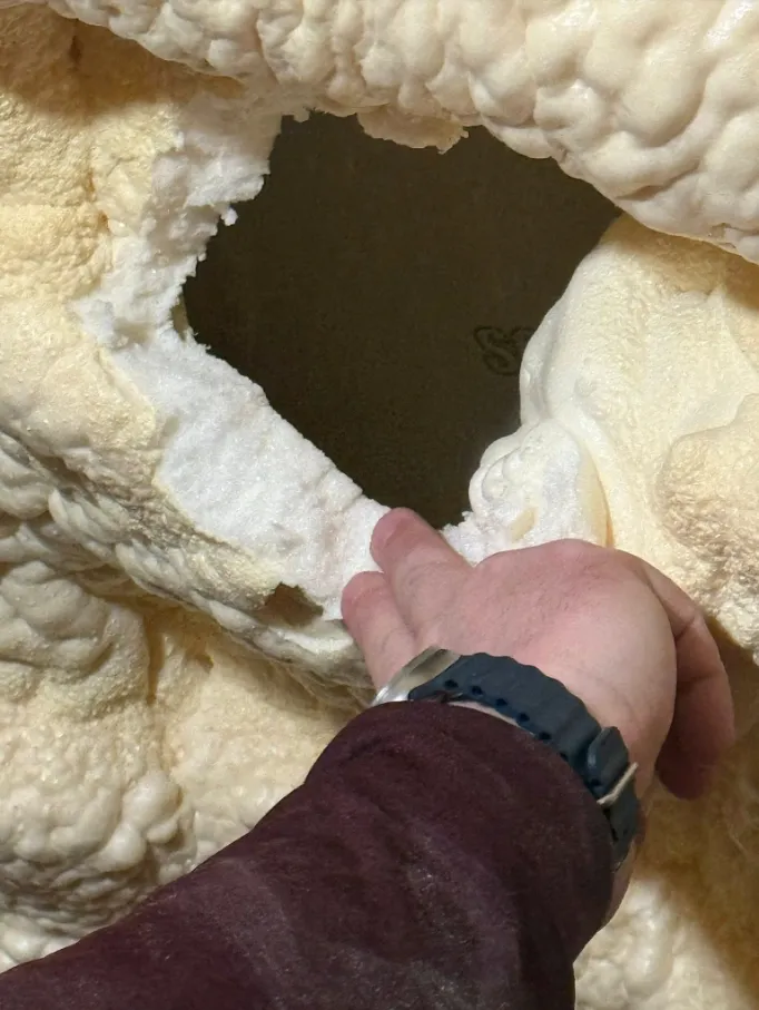 Hand pulling failed spray foam off a roof deck — showing zero adhesion and structural gaps left by a botched installation
