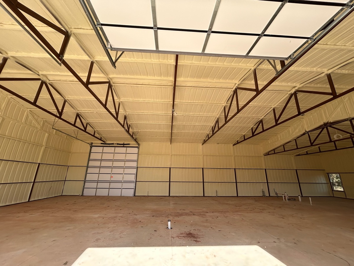 Spray foam insulated metal building with skylight panels allowing natural light — ceiling and walls fully coated.