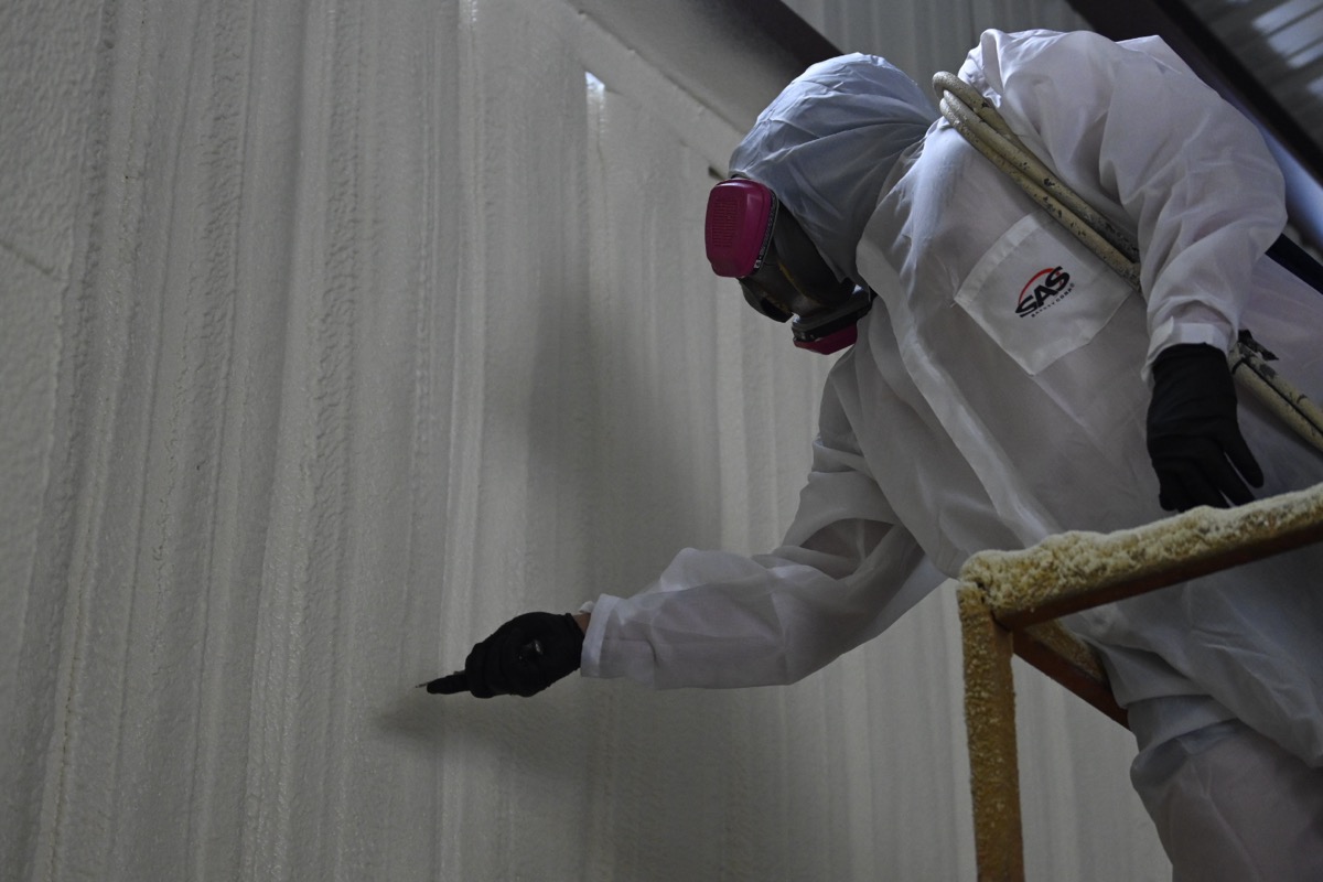Spray foam technician trimming insulation on scaffold for a clean finish