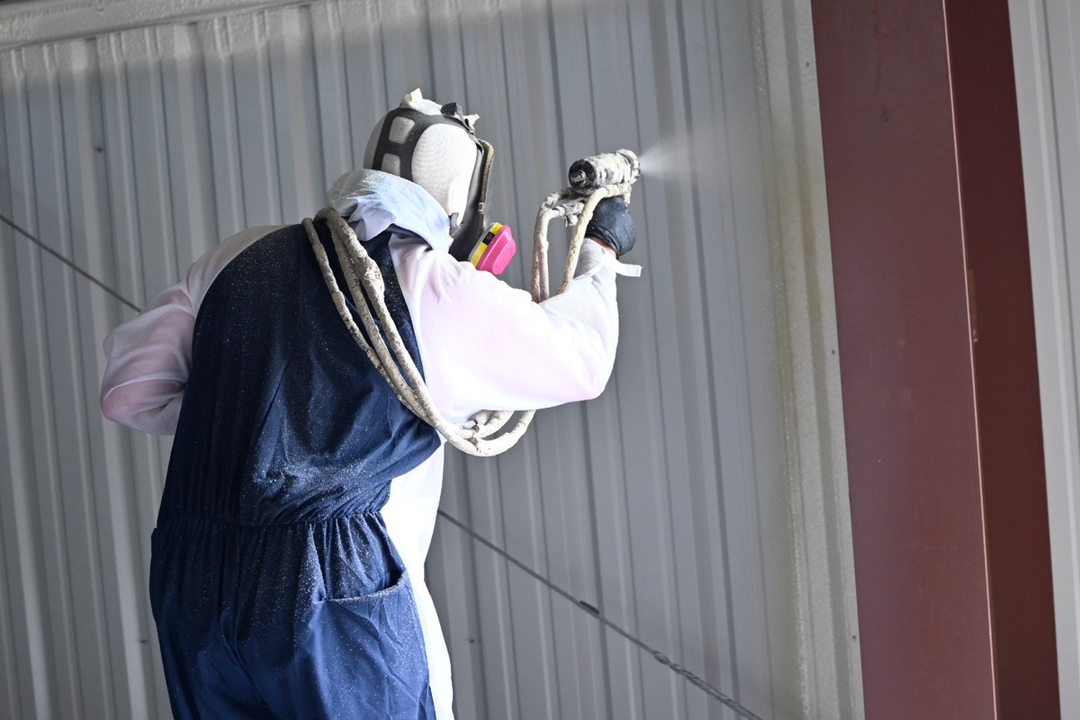 Spray foam technician spraying walls inside a building — safety gear on, foam being applied at correct thickness.